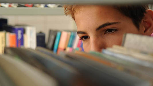 Young man looking to a book shelf 